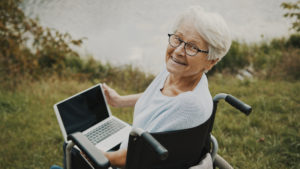 elderly woman sitting in wheel chair with laptop by the water