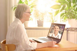 elderly woman on video call with doctor taking notes