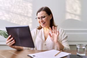 Woman smiling and waving at tablet with notepad
