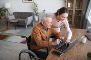 Female care provider helping elderly man on laptop