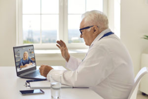 Older male doctor waving at woman on laptop screen