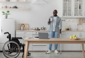 man in kitchen drinking coffee using crutches
