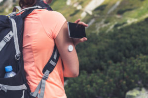 Woman On Mountain With Phone and Diabetes Device